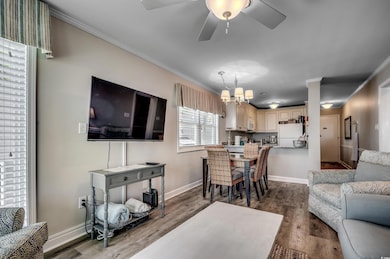 Living room with ceiling fan with notable chandelier, dark hardwood / wood-style flooring, and crown molding