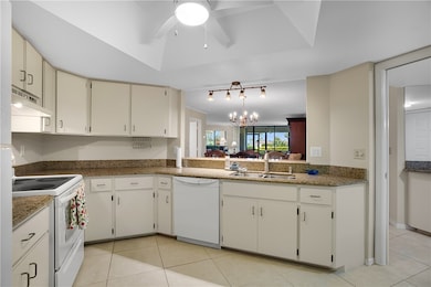 Kitchen with white appliances, a chandelier, light tile patterned flooring, and under cabinet range hood