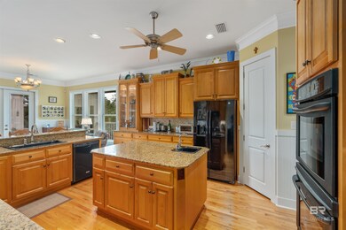 Kitchen with ceiling fan with notable chandelier, black appliances, ornamental molding, a kitchen island with sink, and sink