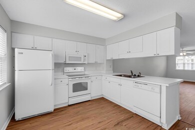Kitchen with a sink, white cabinetry, white appliances, light wood-style floors, and a peninsula
