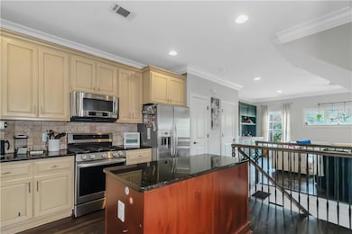 Kitchen with stainless steel appliances, cream cabinets, ornamental molding, dark wood-style floors, and backsplash