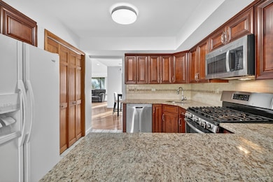 Kitchen with stainless steel appliances, light stone counters, tasteful backsplash, brown cabinets, and light wood finished floors