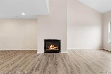 Unfurnished living room with light wood finished floors, a warm lit fireplace, recessed lighting, and high vaulted ceiling