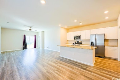 Kitchen with open floor plan, stainless steel appliances, tasteful backsplash, light stone countertops, and white cabinetry