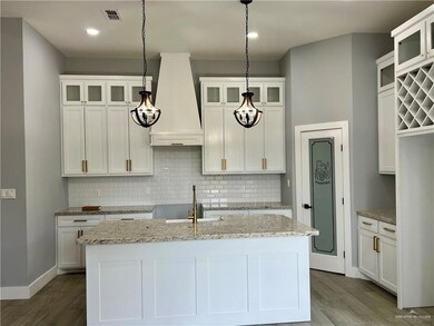 Kitchen with premium range hood, an island with sink, hardwood / wood-style flooring, decorative light fixtures, and white cabinetry
