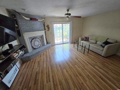 Living room featuring a fireplace, wood finished floors, a textured ceiling, and a ceiling fan