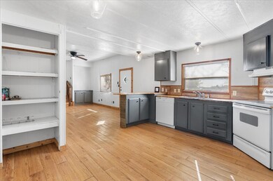 Kitchen featuring gray cabinets, white appliances, a peninsula, light wood-style flooring, and a textured ceiling