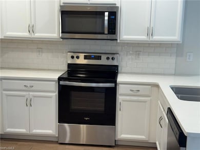 Kitchen with appliances with stainless steel finishes, white cabinetry, light countertops, and backsplash
