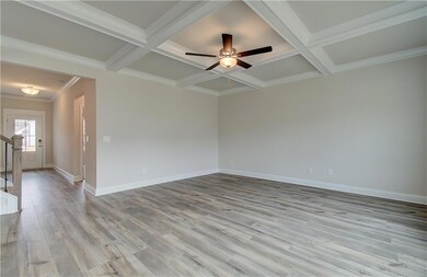 Spare room with coffered ceiling, light wood-style flooring, baseboards, ceiling fan, and beamed ceiling