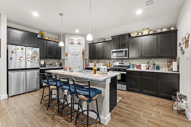 Kitchen with tasteful backsplash, a kitchen breakfast bar, appliances with stainless steel finishes, light stone counters, and decorative light fixtures