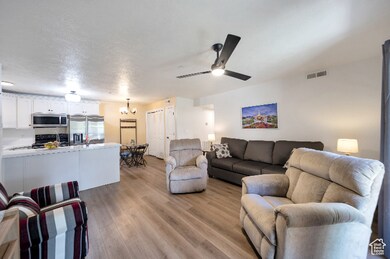 Living room with light wood-style flooring, a chandelier, a textured ceiling, and ceiling fan