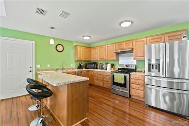 Kitchen featuring appliances with stainless steel finishes, under cabinet range hood, a peninsula, dark wood-style floors, and light countertops