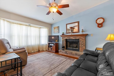 Living area with wood finished floors, a brick fireplace, ceiling fan, and lofted ceiling