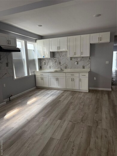 Kitchen featuring white cabinets, backsplash, light wood-style flooring, and exhaust hood
