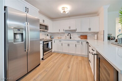 Kitchen featuring stainless steel appliances, white cabinetry, wine cooler, decorative backsplash, and ornamental molding