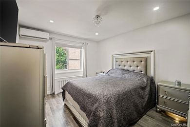 Bedroom with dark wood-style floors, recessed lighting, a wall mounted AC, and freestanding refrigerator