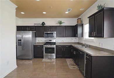 Kitchen with appliances with stainless steel finishes, a sink, ornamental molding, recessed lighting, and tasteful backsplash