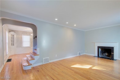 Unfurnished living room featuring crown molding, light wood finished floors, recessed lighting, arched walkways, and a fireplace with flush hearth