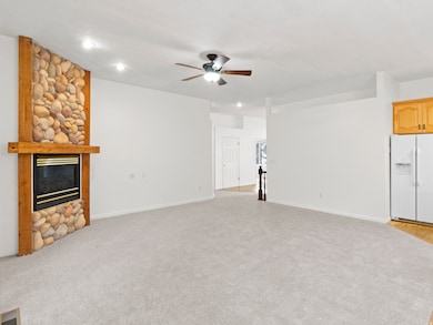 Unfurnished living room featuring a stone fireplace, light colored carpet, a ceiling fan, and recessed lighting