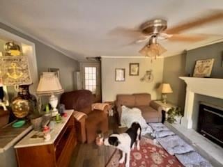 Living area with ornamental molding, wood finished floors, a fireplace with raised hearth, and ceiling fan