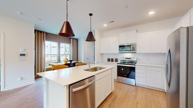 ***This photo was taken from the Grisham model home in Adams Preserve***  The Kitchen includes white cabinetry, quartz countertops and a white beveled subway tile backsplash.