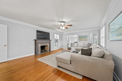 Living room with built in shelves, light wood-style flooring, crown molding, ceiling fan, and a tiled fireplace