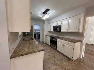 Kitchen with dark stone counters, white cabinetry, electric range, and backsplash