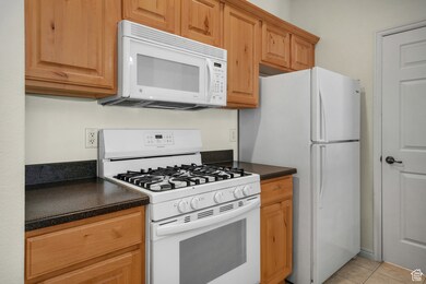 Kitchen with white appliances, dark countertops, and light tile patterned floors