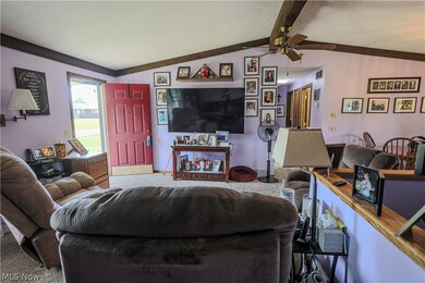 Living room featuring ceiling fan, vaulted ceiling with beams, and carpet flooring