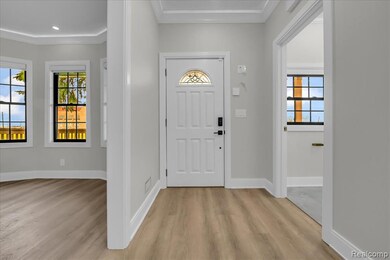 Foyer with healthy amount of natural light, ornamental molding, and light wood-style floors