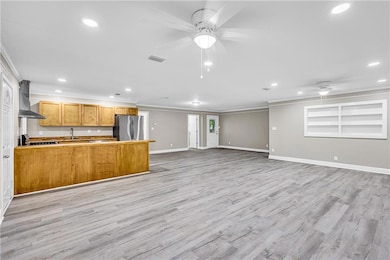 Kitchen with freestanding refrigerator, wall chimney range hood, a ceiling fan, crown molding, and recessed lighting