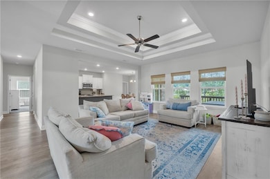 Living area with recessed lighting, light wood finished floors, a ceiling fan, a raised ceiling, and baseboards