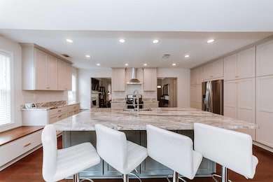Kitchen featuring appliances with stainless steel finishes, wall chimney exhaust hood, a kitchen bar, recessed lighting, and light stone countertops