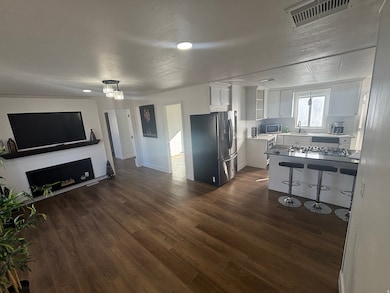 Kitchen with white cabinetry, a kitchen bar, stainless steel appliances, open floor plan, and dark wood-style floors