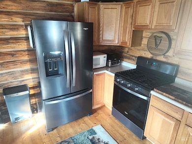 Kitchen with gas stove, stainless steel refrigerator with ice dispenser, white microwave, light wood-style flooring, and light countertops