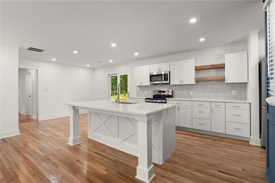 Kitchen with a sink, stainless steel appliances, open shelves, backsplash, and white cabinetry