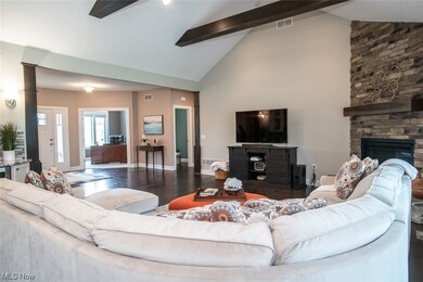Living room with high vaulted ceiling, a stone fireplace, beam ceiling, and dark wood-type flooring