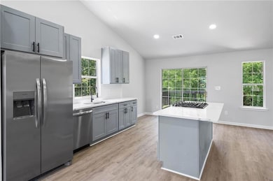 Kitchen with stainless steel appliances, a sink, lofted ceiling, gray cabinetry, and light wood-style floors