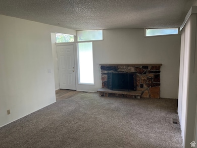 Unfurnished living room featuring a stone fireplace, carpet, and a textured ceiling