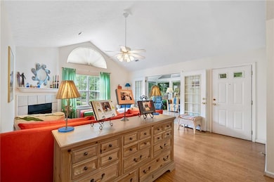Living area with lofted ceiling, ceiling fan, light wood-style floors, and a fireplace