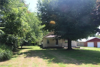 View of green lawn with a detached garage, a porch, an outbuilding, and driveway