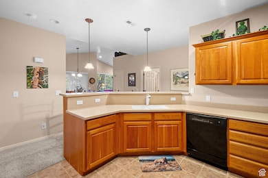 Kitchen featuring brown cabinets, a peninsula, vaulted ceiling, dishwasher, and decorative light fixtures