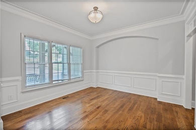 Spare room with ornamental molding, wood finished floors, wainscoting, and a decorative wall