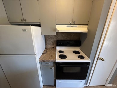 Kitchen with range with electric cooktop, backsplash, under cabinet range hood, and freestanding refrigerator