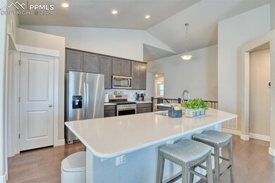 Kitchen featuring pendant lighting, lofted ceiling, stainless steel appliances, and an island with sink