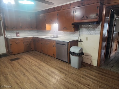 Kitchen featuring decorative backsplash, light countertops, wood finished floors, stainless steel dishwasher, and under cabinet range hood