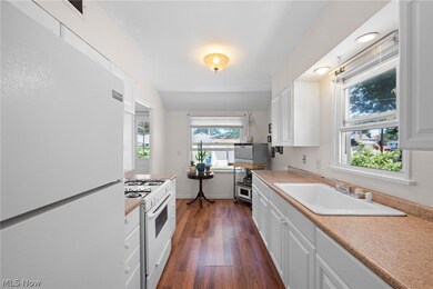 Kitchen with sink, white appliances, white cabinetry, and dark wood-type flooring