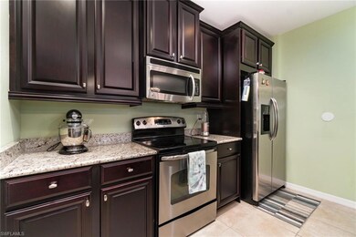 Kitchen with appliances with stainless steel finishes, dark brown cabinets, baseboards, light tile patterned flooring, and light stone countertops