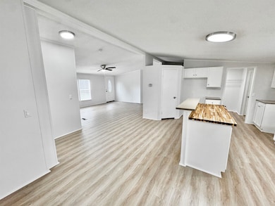 Kitchen with a textured ceiling, light wood-type flooring, white cabinetry, wood counters, and a kitchen island