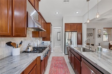 Kitchen with decorative backsplash, hanging light fixtures, appliances with stainless steel finishes, light stone countertops, and recessed lighting
